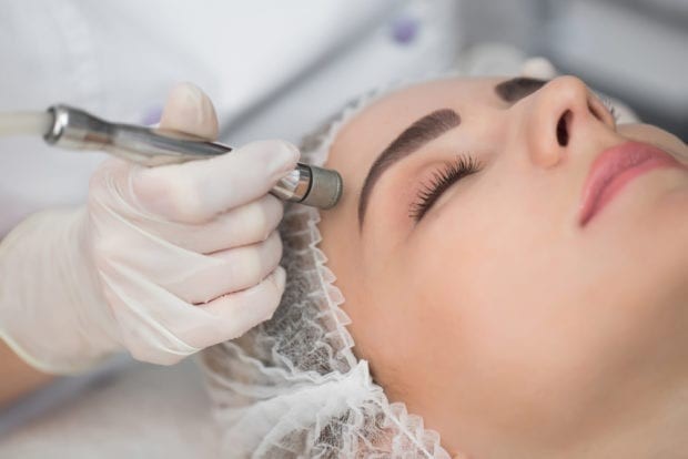A Microdermabrasion Wand Being Dragged Across a Hair-netted Woman’s Forehead